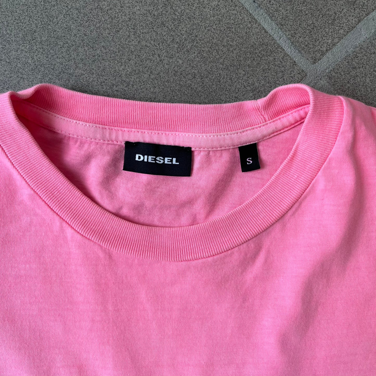 Diesel DLVERANCE Bright Pink Tee features a 100% cotton jersey construction with a fluorescent pink pigment-dyed finish. The front has a rubberised “DLVERANCE” graphic, with a small rubber “Copyright” logo on the lower back.