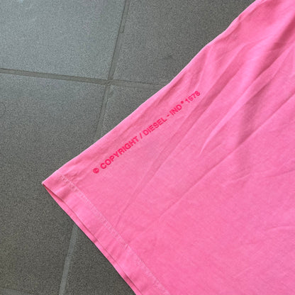 Diesel DLVERANCE Bright Pink Tee features a 100% cotton jersey construction with a fluorescent pink pigment-dyed finish. The front has a rubberised “DLVERANCE” graphic, with a small rubber “Copyright” logo on the lower back.