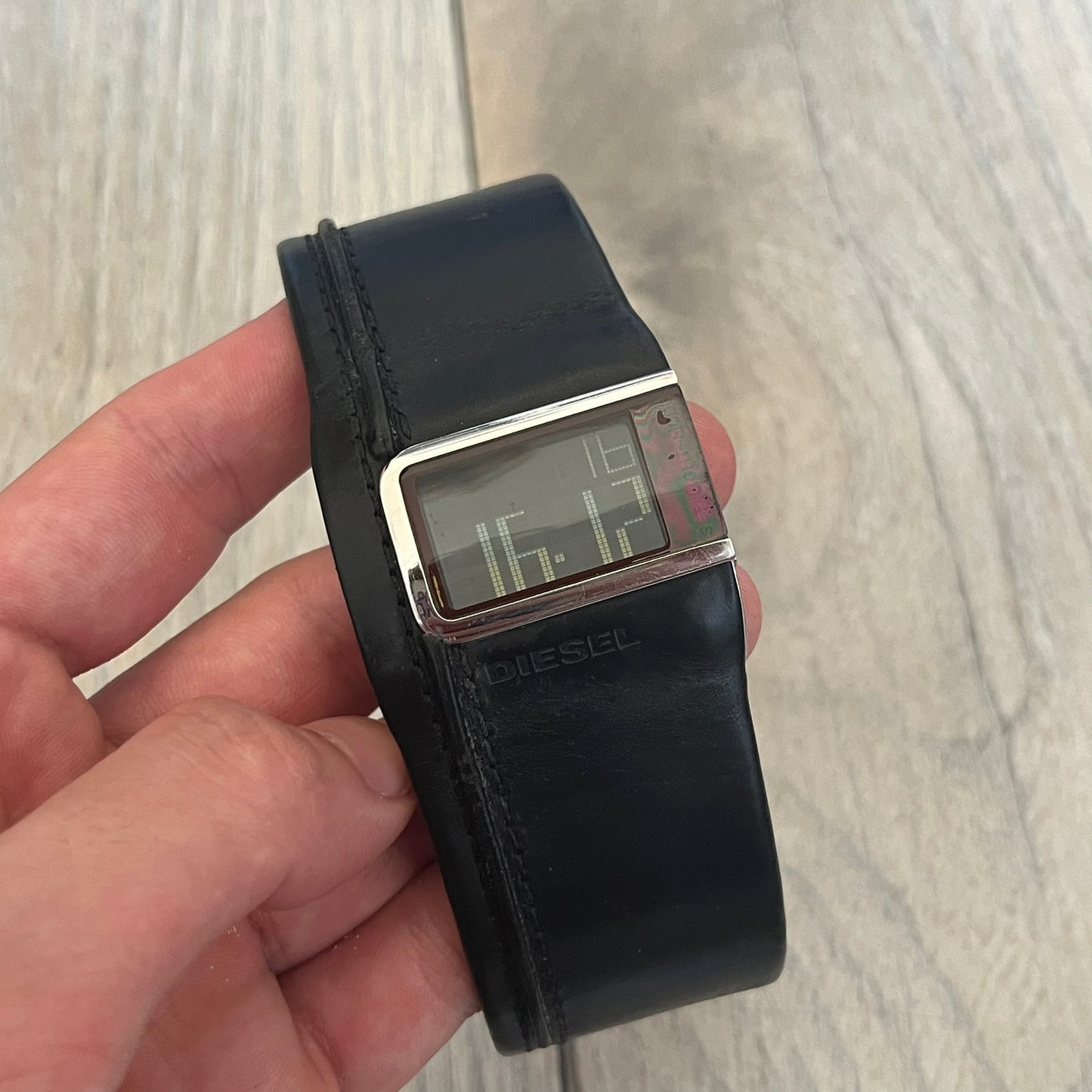 Diesel DZ7033 Black Leather Strap Digital Watch features a Black leather strap and a black digital display housed in a silver rectangular case. The watch includes a backlight, Arabic numeral indices, and a deployant closure, with a stainless steel case back engraved with Diesel branding and model number DZ-7090. It is water resistant up to 50 meters (5 ATM) and combines industrial design with functional quartz digital movement.&nbsp;