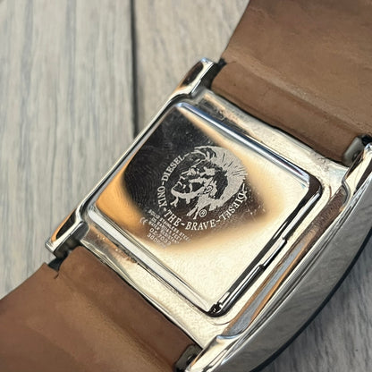 Diesel DZ7033 Black Leather Strap Digital Watch features a Black leather strap and a black digital display housed in a silver rectangular case. The watch includes a backlight, Arabic numeral indices, and a deployant closure, with a stainless steel case back engraved with Diesel branding and model number DZ-7090. It is water resistant up to 50 meters (5 ATM) and combines industrial design with functional quartz digital movement.&nbsp;