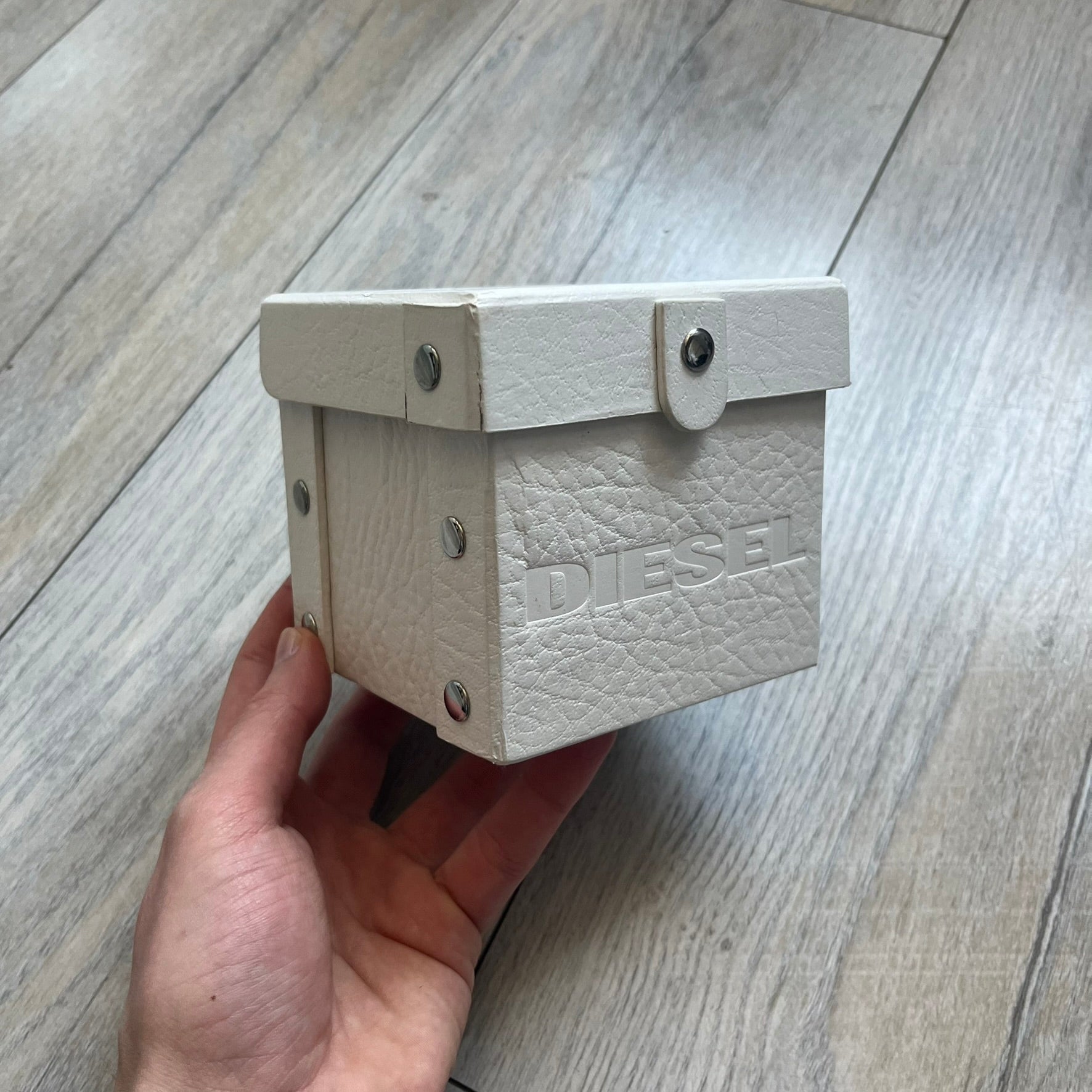 Diesel DZ7068 Studded Leather Strap Digital Watch features a white leather patchwork strap accented with small metal studs and a black digital display housed in a silver rectangular case. The watch includes a backlight, Arabic numeral indices, and a deployant closure, with a stainless steel case back engraved with Diesel branding and model number DZ-7068. It is water resistant up to 50 meters (5 ATM) and combines industrial design with functional quartz digital movement.