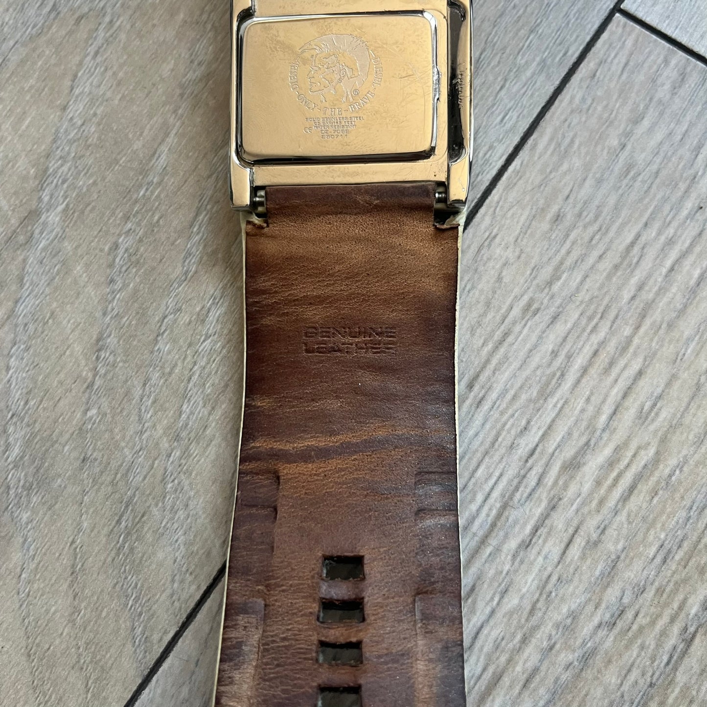 Diesel DZ7068 Studded Leather Strap Digital Watch features a white leather patchwork strap accented with small metal studs and a black digital display housed in a silver rectangular case. The watch includes a backlight, Arabic numeral indices, and a deployant closure, with a stainless steel case back engraved with Diesel branding and model number DZ-7068. It is water resistant up to 50 meters (5 ATM) and combines industrial design with functional quartz digital movement.