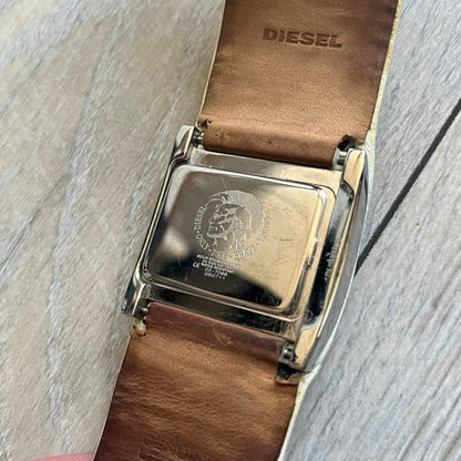 Diesel DZ7068 Studded Leather Strap Digital Watch features a white leather patchwork strap accented with small metal studs and a black digital display housed in a silver rectangular case. The watch includes a backlight, Arabic numeral indices, and a deployant closure, with a stainless steel case back engraved with Diesel branding and model number DZ-7068. It is water resistant up to 50 meters (5 ATM) and combines industrial design with functional quartz digital movement.