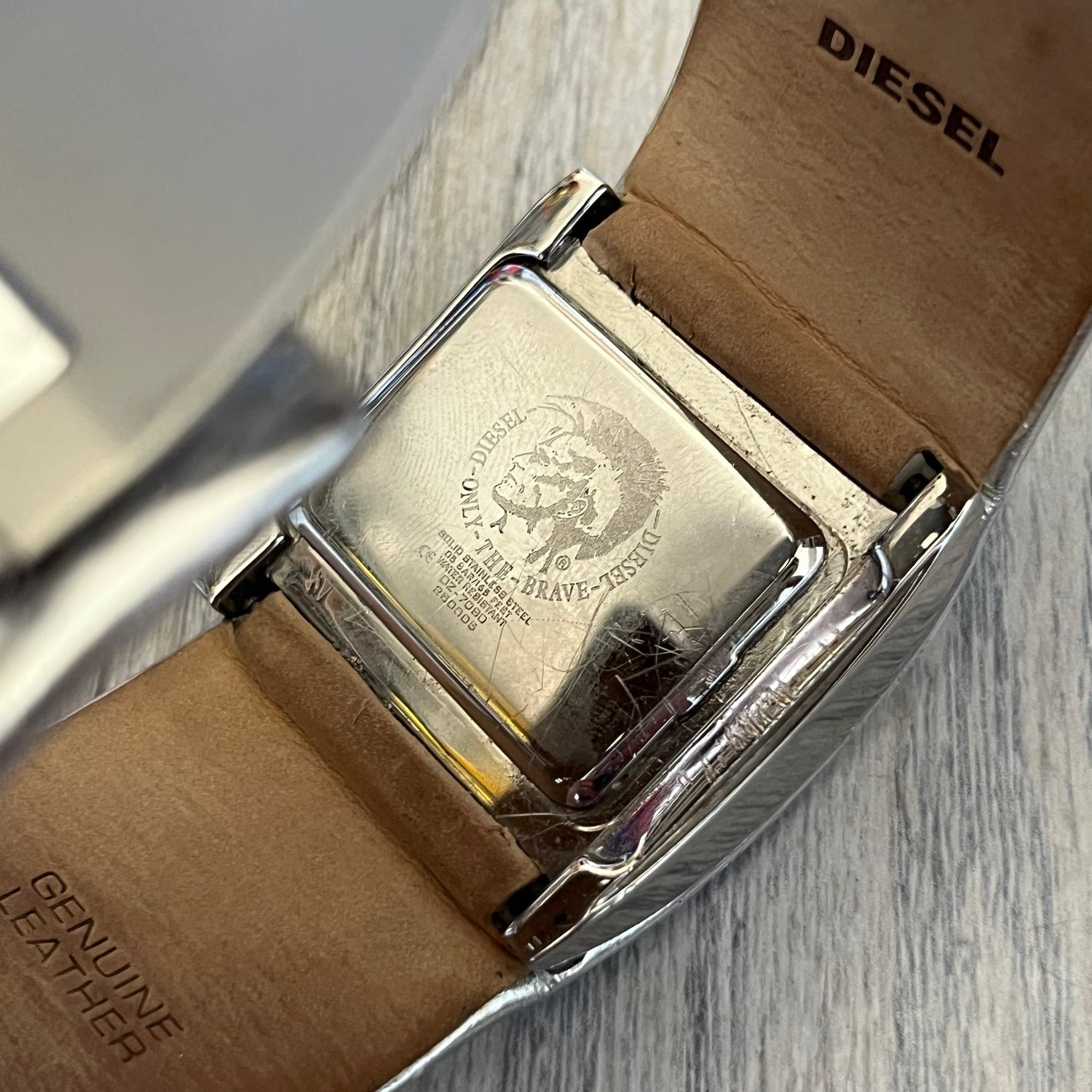 Diesel DZ7090 Silver Leather Strap Digital Watch features a Silver leather patchwork strap and a black digital display housed in a silver rectangular case. The watch includes a backlight, Arabic numeral indices, and a deployant closure, with a stainless steel case back engraved with Diesel branding and model number DZ-7090. It is water resistant up to 50 meters (5 ATM) and combines industrial design with functional quartz digital movement.&nbsp;