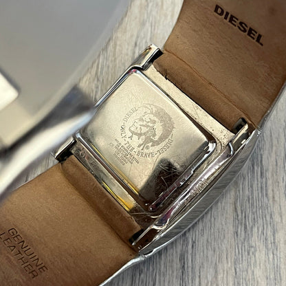 Diesel DZ7090 Silver Leather Strap Digital Watch features a Silver leather patchwork strap and a black digital display housed in a silver rectangular case. The watch includes a backlight, Arabic numeral indices, and a deployant closure, with a stainless steel case back engraved with Diesel branding and model number DZ-7090. It is water resistant up to 50 meters (5 ATM) and combines industrial design with functional quartz digital movement.&nbsp;