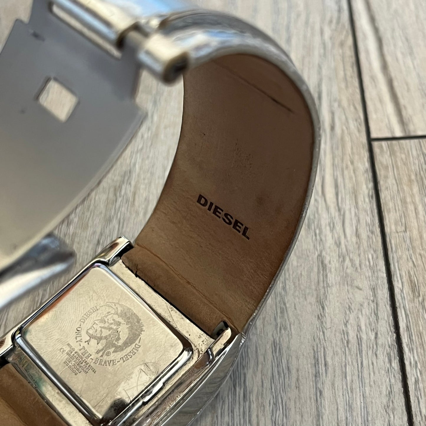 Diesel DZ7090 Silver Leather Strap Digital Watch features a Silver leather patchwork strap and a black digital display housed in a silver rectangular case. The watch includes a backlight, Arabic numeral indices, and a deployant closure, with a stainless steel case back engraved with Diesel branding and model number DZ-7090. It is water resistant up to 50 meters (5 ATM) and combines industrial design with functional quartz digital movement.&nbsp;