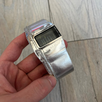 Diesel DZ7090 Silver Leather Strap Digital Watch features a Silver leather patchwork strap and a black digital display housed in a silver rectangular case. The watch includes a backlight, Arabic numeral indices, and a deployant closure, with a stainless steel case back engraved with Diesel branding and model number DZ-7090. It is water resistant up to 50 meters (5 ATM) and combines industrial design with functional quartz digital movement.&nbsp;
