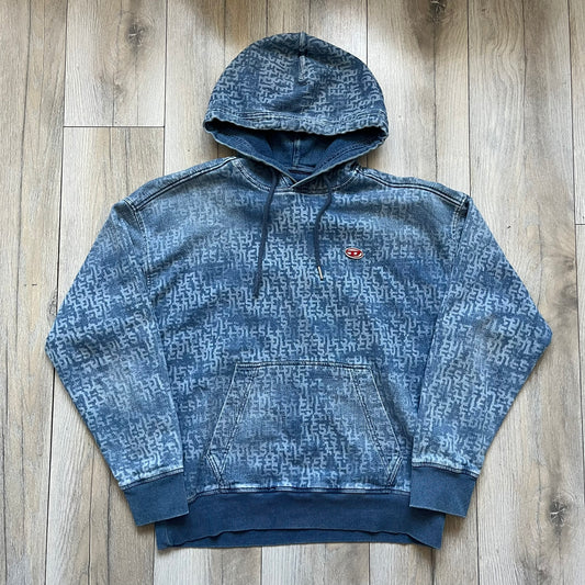Diesel “Denim” Logo Blue Hoodie is a blue hooded sweatshirt designed with a denim-inspired colorway and washed effect throughout. The fabric features varying light and dark blue shades to mimic the appearance of worn denim, along with an all-over Diesel text pattern in a slightly lighter tone. A small red Diesel patch is placed on the chest, while the cuffs and hem are finished in a contrasting navy color.