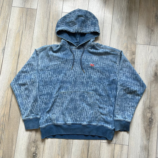 Diesel “Denim” Logo Blue Hoodie is a blue hooded sweatshirt designed with a denim-inspired colorway and washed effect throughout. The fabric features varying light and dark blue shades to mimic the appearance of worn denim, along with an all-over Diesel text pattern in a slightly lighter tone. A small red Diesel patch is placed on the chest, while the cuffs and hem are finished in a contrasting navy color.&nbsp;