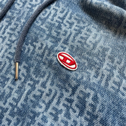 Diesel “Denim” Logo Blue Hoodie is a blue hooded sweatshirt designed with a denim-inspired colorway and washed effect throughout. The fabric features varying light and dark blue shades to mimic the appearance of worn denim, along with an all-over Diesel text pattern in a slightly lighter tone. A small red Diesel patch is placed on the chest, while the cuffs and hem are finished in a contrasting navy color.&nbsp;