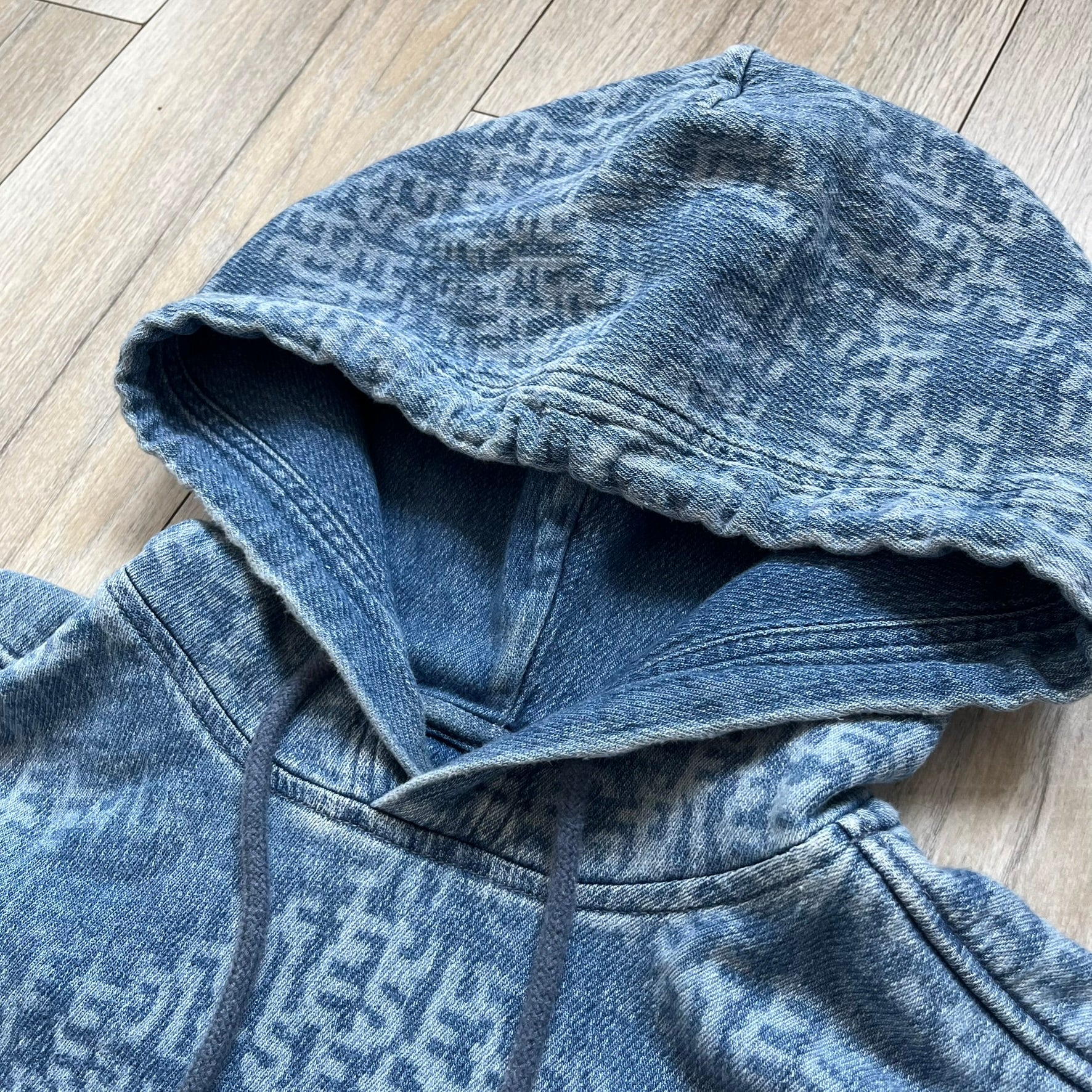 Diesel “Denim” Logo Blue Hoodie is a blue hooded sweatshirt designed with a denim-inspired colorway and washed effect throughout. The fabric features varying light and dark blue shades to mimic the appearance of worn denim, along with an all-over Diesel text pattern in a slightly lighter tone. A small red Diesel patch is placed on the chest, while the cuffs and hem are finished in a contrasting navy color.&nbsp;