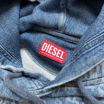 Diesel “Denim” Logo Blue Hoodie is a blue hooded sweatshirt designed with a denim-inspired colorway and washed effect throughout. The fabric features varying light and dark blue shades to mimic the appearance of worn denim, along with an all-over Diesel text pattern in a slightly lighter tone. A small red Diesel patch is placed on the chest, while the cuffs and hem are finished in a contrasting navy color.&nbsp;