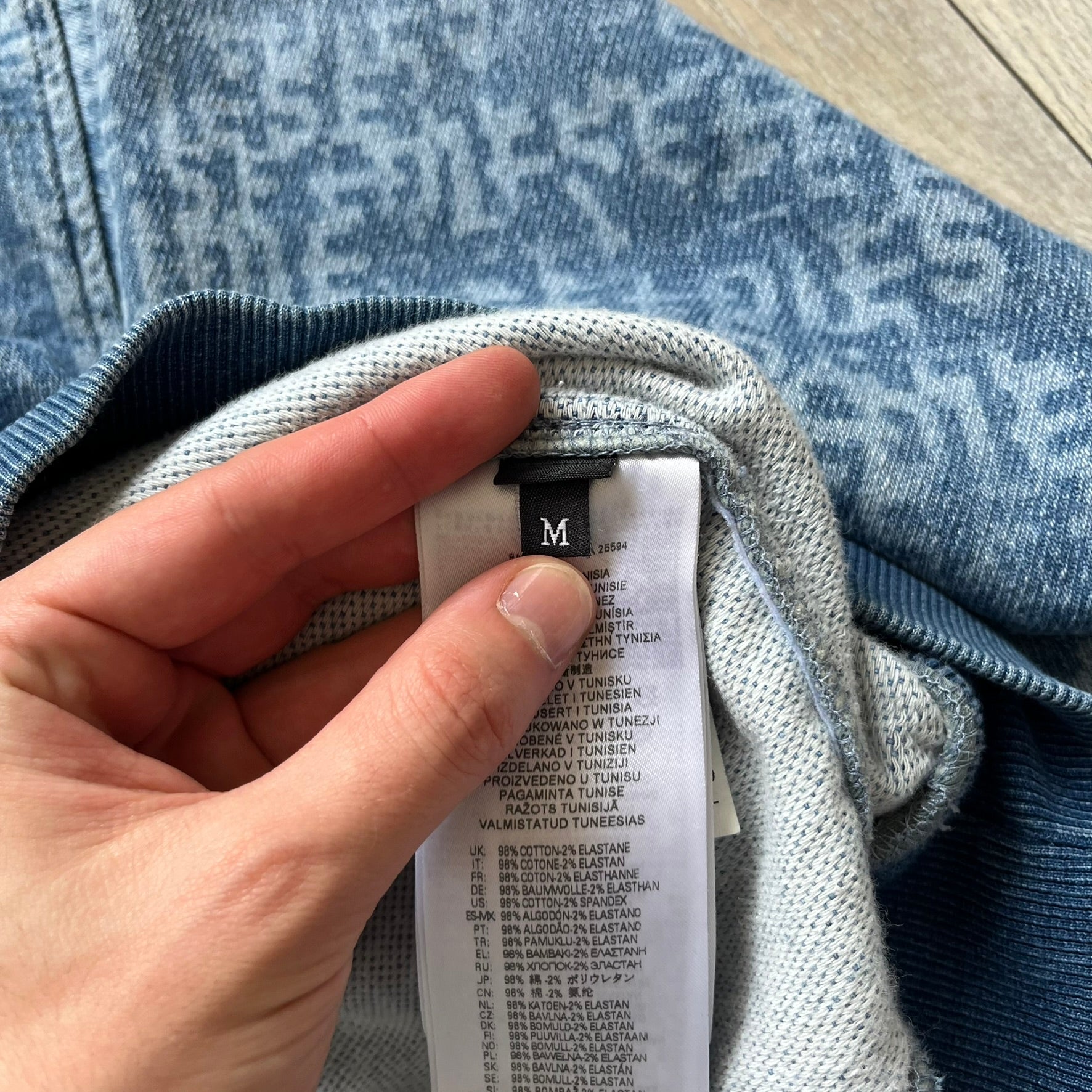 Diesel “Denim” Logo Blue Hoodie is a blue hooded sweatshirt designed with a denim-inspired colorway and washed effect throughout. The fabric features varying light and dark blue shades to mimic the appearance of worn denim, along with an all-over Diesel text pattern in a slightly lighter tone. A small red Diesel patch is placed on the chest, while the cuffs and hem are finished in a contrasting navy color.&nbsp;