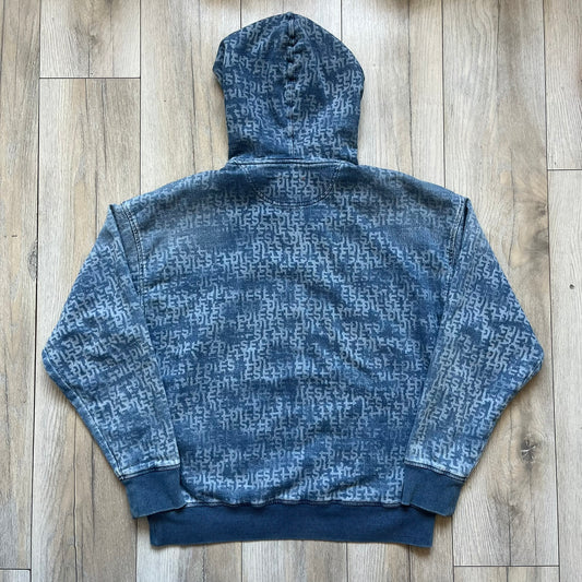 Diesel “Denim” Logo Blue Hoodie is a blue hooded sweatshirt designed with a denim-inspired colorway and washed effect throughout. The fabric features varying light and dark blue shades to mimic the appearance of worn denim, along with an all-over Diesel text pattern in a slightly lighter tone. A small red Diesel patch is placed on the chest, while the cuffs and hem are finished in a contrasting navy color.