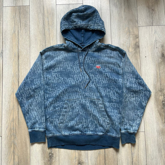 Diesel “Denim” Logo Blue Hoodie is a blue hooded sweatshirt designed with a denim-inspired colorway and washed effect throughout. The fabric features varying light and dark blue shades to mimic the appearance of worn denim, along with an all-over Diesel text pattern in a slightly lighter tone. A small red Diesel patch is placed on the chest, while the cuffs and hem are finished in a contrasting navy color.&nbsp;