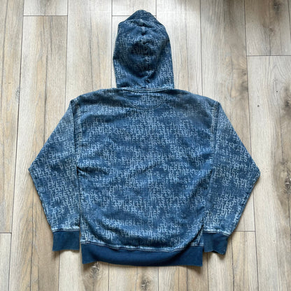 Diesel “Denim” Logo Blue Hoodie is a blue hooded sweatshirt designed with a denim-inspired colorway and washed effect throughout. The fabric features varying light and dark blue shades to mimic the appearance of worn denim, along with an all-over Diesel text pattern in a slightly lighter tone. A small red Diesel patch is placed on the chest, while the cuffs and hem are finished in a contrasting navy color.&nbsp;