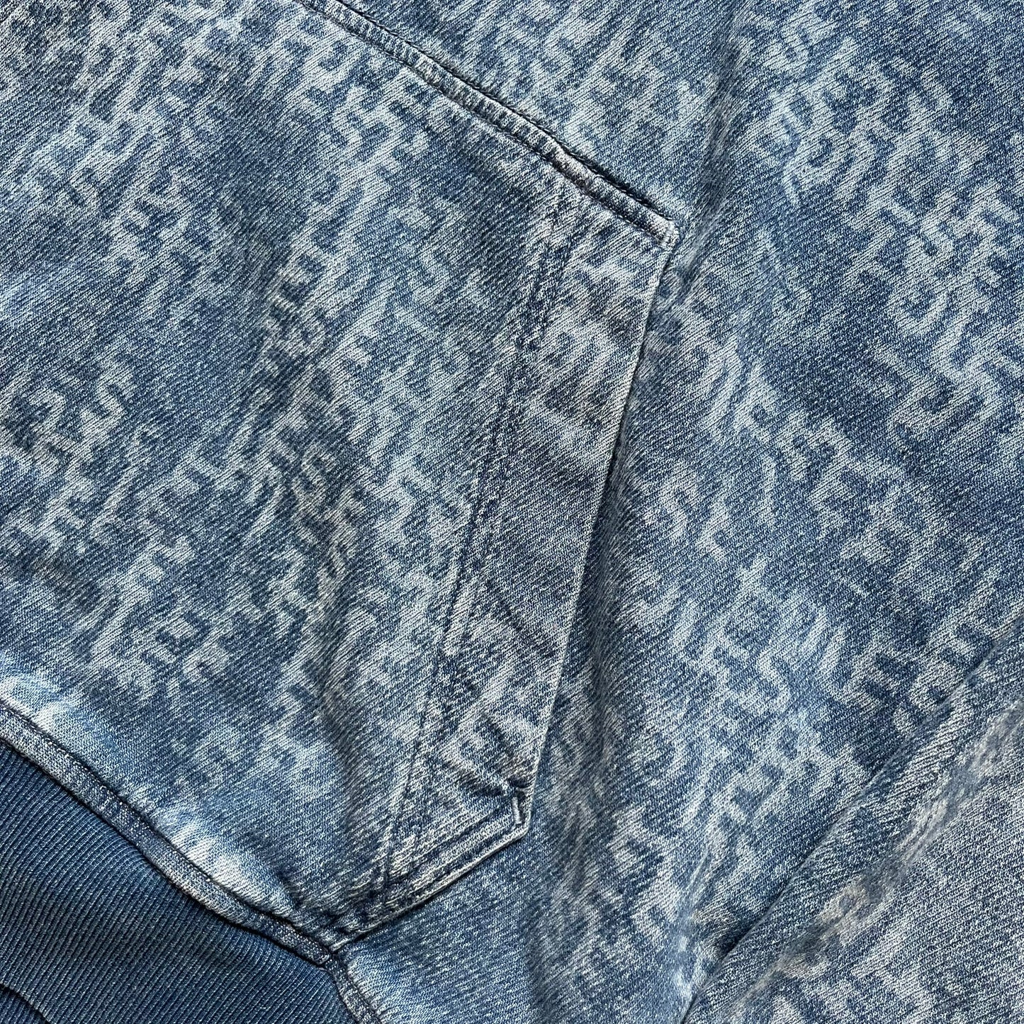 Diesel “Denim” Logo Blue Hoodie is a blue hooded sweatshirt designed with a denim-inspired colorway and washed effect throughout. The fabric features varying light and dark blue shades to mimic the appearance of worn denim, along with an all-over Diesel text pattern in a slightly lighter tone. A small red Diesel patch is placed on the chest, while the cuffs and hem are finished in a contrasting navy color.&nbsp;