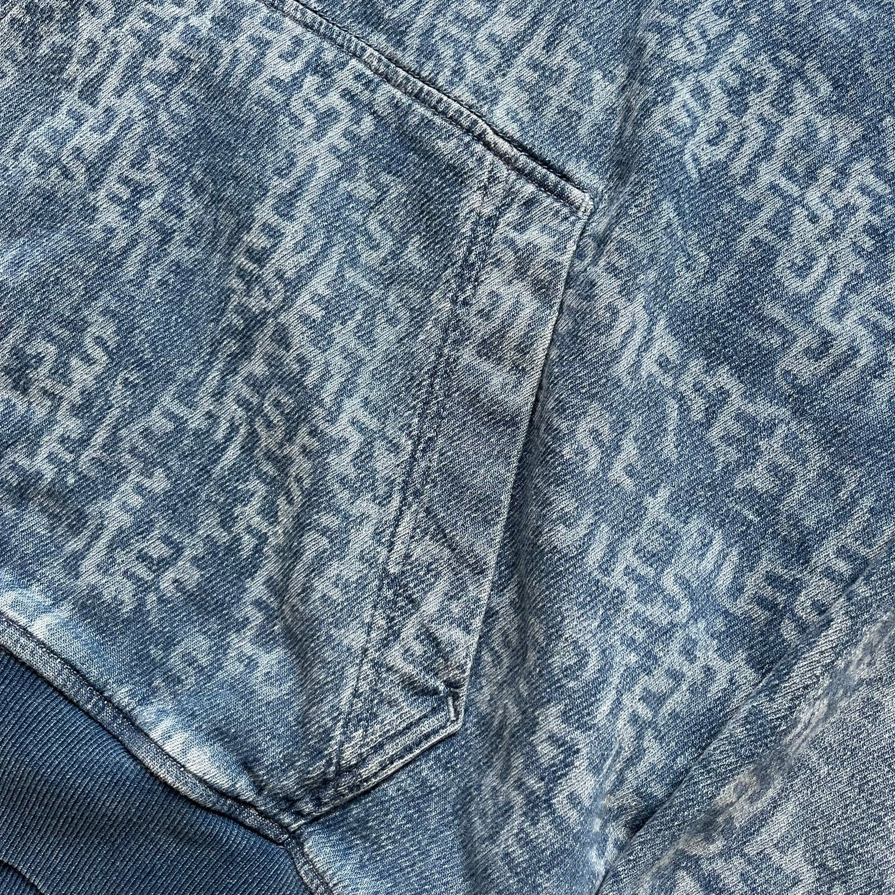 Diesel “Denim” Logo Blue Hoodie is a blue hooded sweatshirt designed with a denim-inspired colorway and washed effect throughout. The fabric features varying light and dark blue shades to mimic the appearance of worn denim, along with an all-over Diesel text pattern in a slightly lighter tone. A small red Diesel patch is placed on the chest, while the cuffs and hem are finished in a contrasting navy color.&nbsp;
