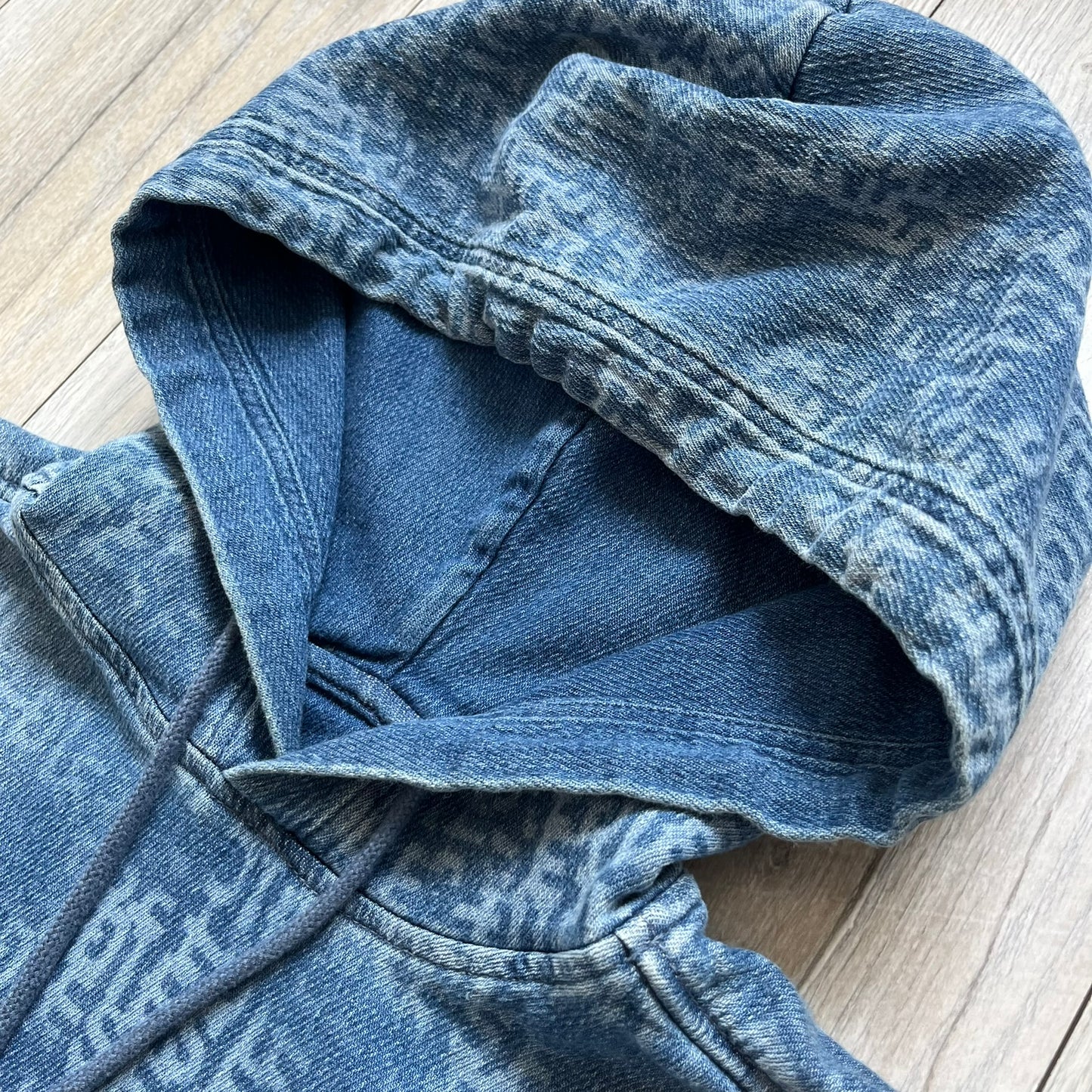 Diesel “Denim” Logo Blue Hoodie is a blue hooded sweatshirt designed with a denim-inspired colorway and washed effect throughout. The fabric features varying light and dark blue shades to mimic the appearance of worn denim, along with an all-over Diesel text pattern in a slightly lighter tone. A small red Diesel patch is placed on the chest, while the cuffs and hem are finished in a contrasting navy color.&nbsp;