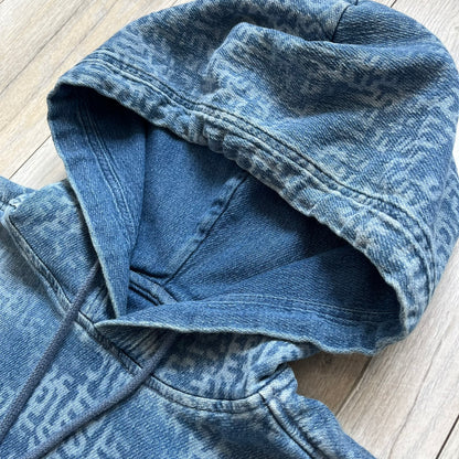 Diesel “Denim” Logo Blue Hoodie is a blue hooded sweatshirt designed with a denim-inspired colorway and washed effect throughout. The fabric features varying light and dark blue shades to mimic the appearance of worn denim, along with an all-over Diesel text pattern in a slightly lighter tone. A small red Diesel patch is placed on the chest, while the cuffs and hem are finished in a contrasting navy color.&nbsp;