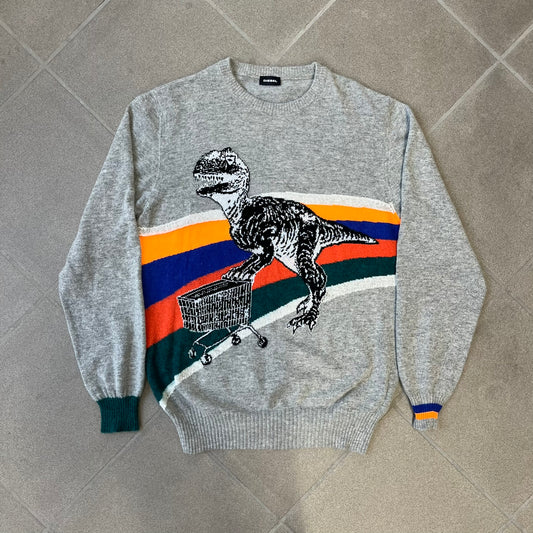 Diesel K-Dino FW19 Gray Pullover is a lightweight gray knit pullover made from alpaca, polyamide, and other materials. The front features a white and black T-rex with a shopping cart, set against multicolor orange, blue, red, and green stripes running behind it.