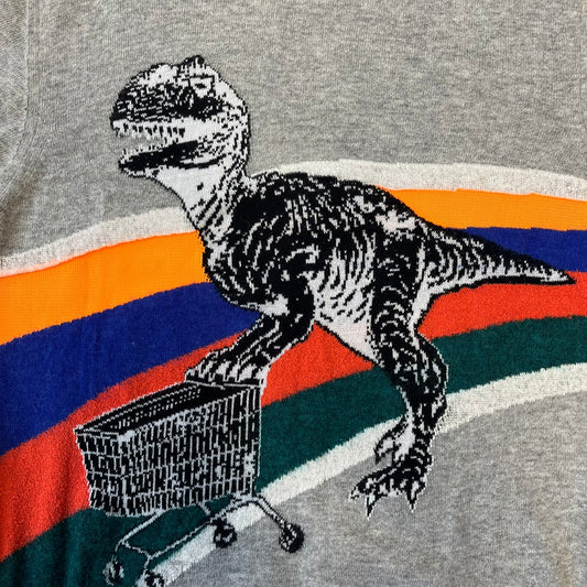Diesel K-Dino FW19 Gray Pullover is a lightweight gray knit pullover made from alpaca, polyamide, and other materials. The front features a white and black T-rex with a shopping cart, set against multicolor orange, blue, red, and green stripes running behind it.