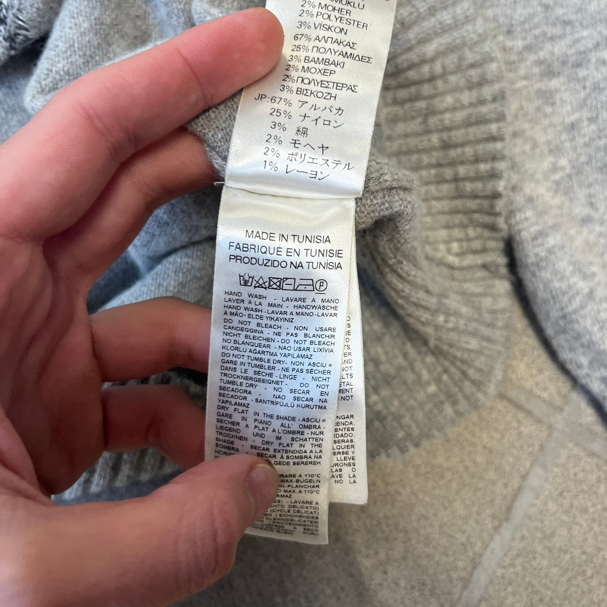 Diesel K-Dino FW19 Gray Pullover is a lightweight gray knit pullover made from alpaca, polyamide, and other materials. The front features a white and black T-rex with a shopping cart, set against multicolor orange, blue, red, and green stripes running behind it.