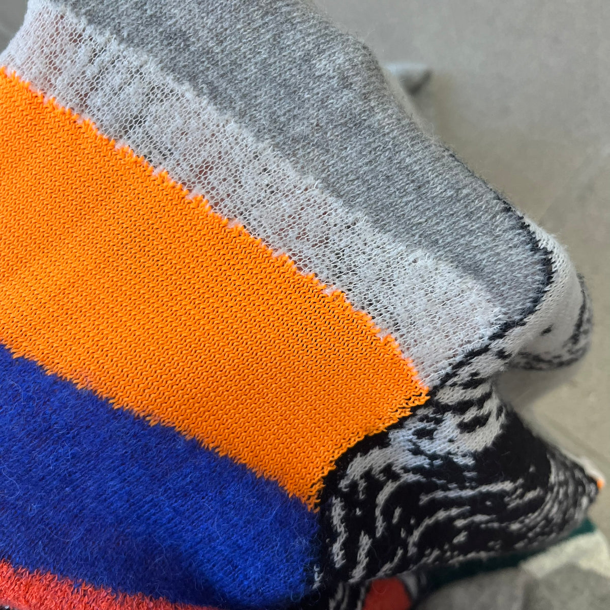 Diesel K-Dino FW19 Gray Pullover is a lightweight gray knit pullover made from alpaca, polyamide, and other materials. The front features a white and black T-rex with a shopping cart, set against multicolor orange, blue, red, and green stripes running behind it.