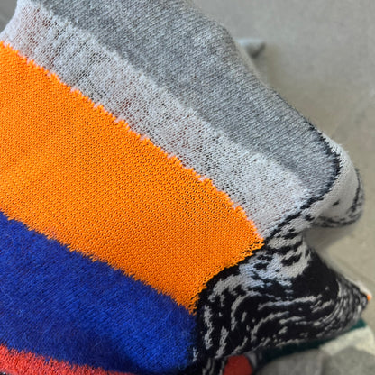 Diesel K-Dino FW19 Gray Pullover is a lightweight gray knit pullover made from alpaca, polyamide, and other materials. The front features a white and black T-rex with a shopping cart, set against multicolor orange, blue, red, and green stripes running behind it.