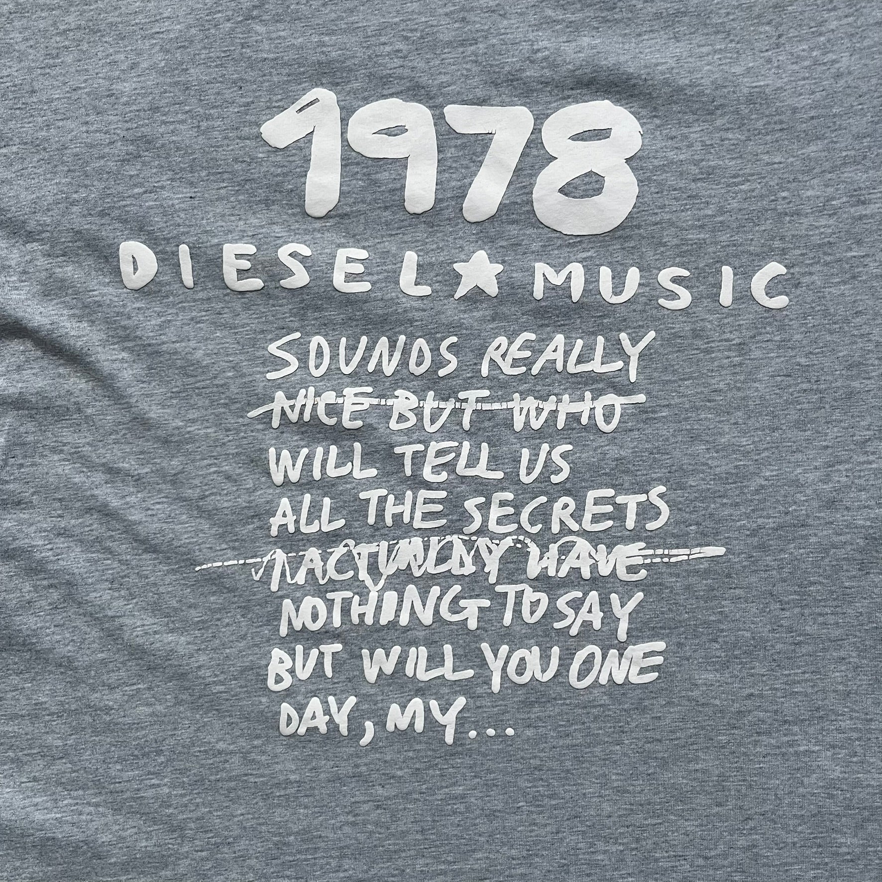 Diesel Music 1978 Gray Tee is a gray T-shirt featuring a large hand-drawn style “Diesel Music 1978” print on the front with additional text below. Made from 100% cotton, it has a crew neckline and short sleeves. The print is white, contrasting with the gray fabric.