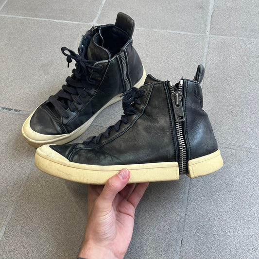 Diesel Zip-Round S-Nentish Black Sneakers feature a high-top silhouette with a black leather upper and a white rubber sole. The sneakers have a full-length zipper detail around the ankle area, running from the top of the shoe down and around the sides. The design includes a lace-up front and Diesel branding details.