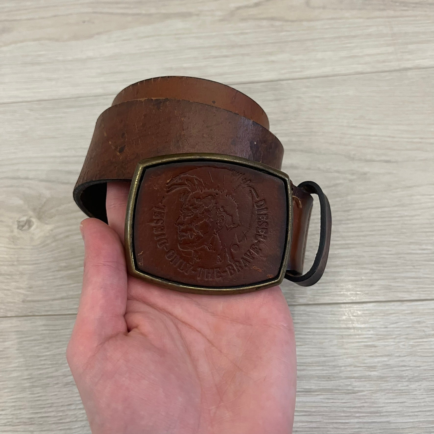 Diesel “Only The Brave” leather belt crafted in Italy from 100% brown leather and finished with a metal buckle with leather front. The buckle displays the Mohawk Warrior helmet motif with surrounding Diesel branding for an iconic look.