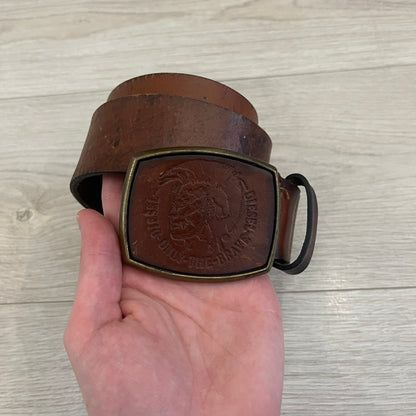 Diesel “Only The Brave” leather belt crafted in Italy from 100% brown leather and finished with a metal buckle with leather front. The buckle displays the Mohawk Warrior helmet motif with surrounding Diesel branding for an iconic look.