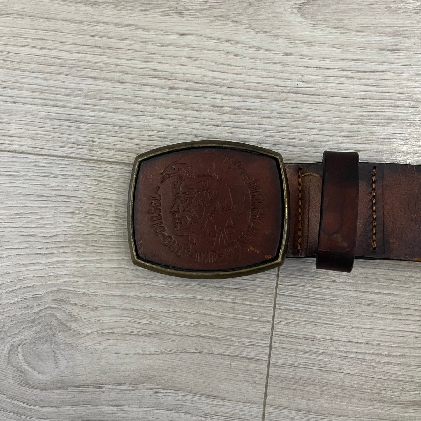 Diesel “Only The Brave” leather belt crafted in Italy from 100% brown leather and finished with a metal buckle with leather front. The buckle displays the Mohawk Warrior helmet motif with surrounding Diesel branding for an iconic look.