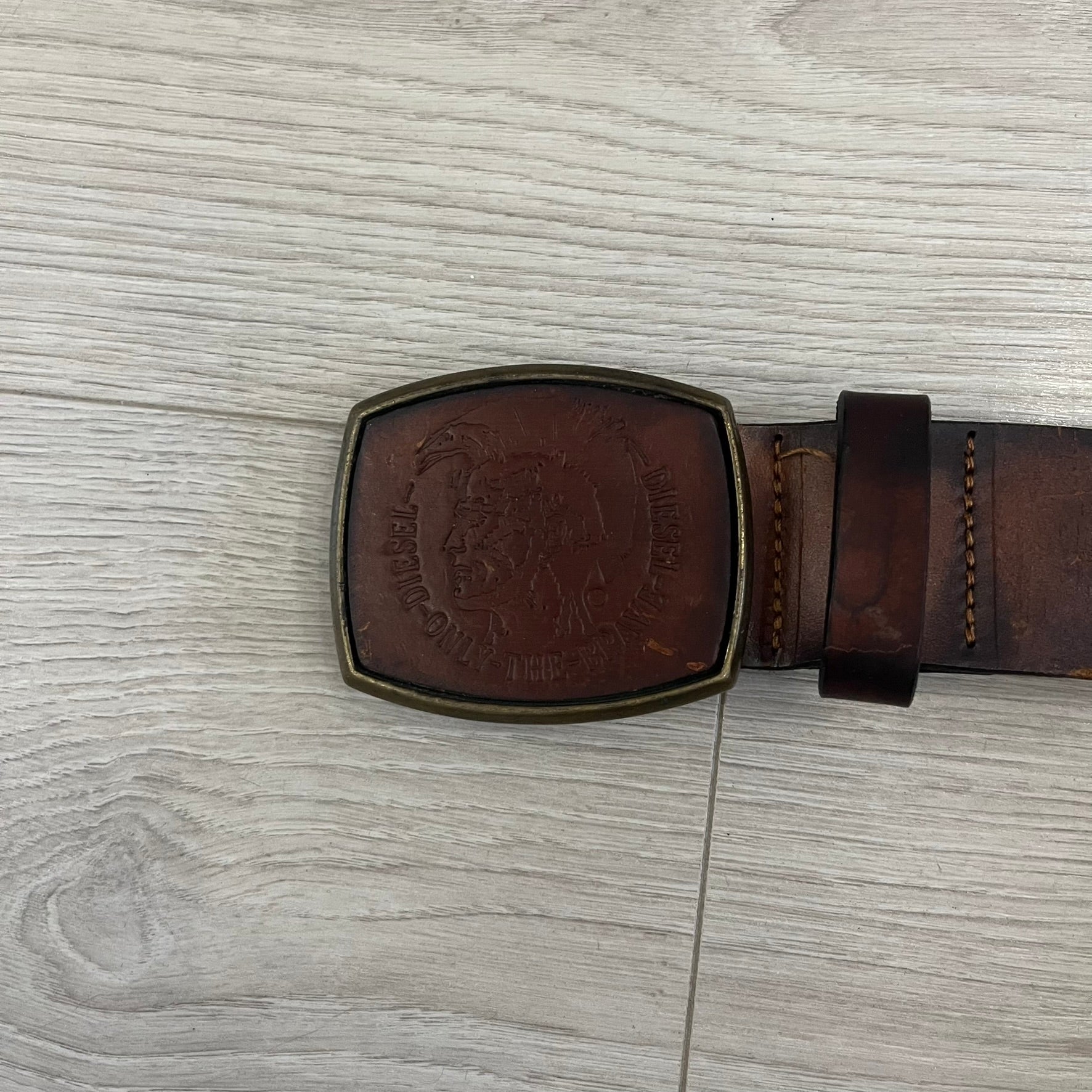 Diesel “Only The Brave” leather belt crafted in Italy from 100% brown leather and finished with a metal buckle with leather front. The buckle displays the Mohawk Warrior helmet motif with surrounding Diesel branding for an iconic look.