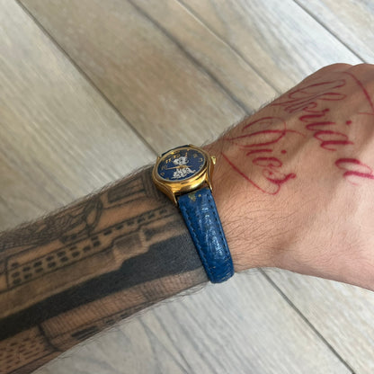 Disney 101 Dalmatians 1990s Blue Analog Watch features a navy leather strap, gold-tone case, and navy dial. The dial includes gold hour markers and hands with a Dalmatian character graphic in the center. The case back is marked as made exclusively for the Disney Store and includes a Japan movement marking. The watch is sized for smaller wrists.
