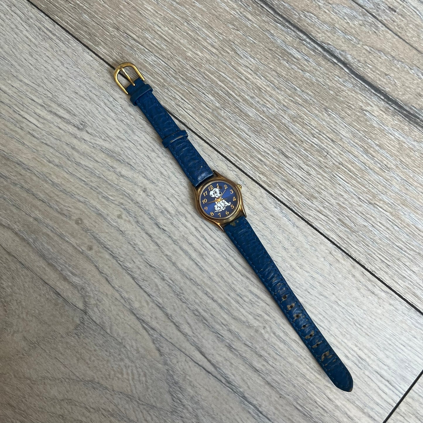 Disney 101 Dalmatians 1990s Blue Analog Watch features a navy leather strap, gold-tone case, and navy dial. The dial includes gold hour markers and hands with a Dalmatian character graphic in the center. The case back is marked as made exclusively for the Disney Store and includes a Japan movement marking. The watch is sized for smaller wrists.
