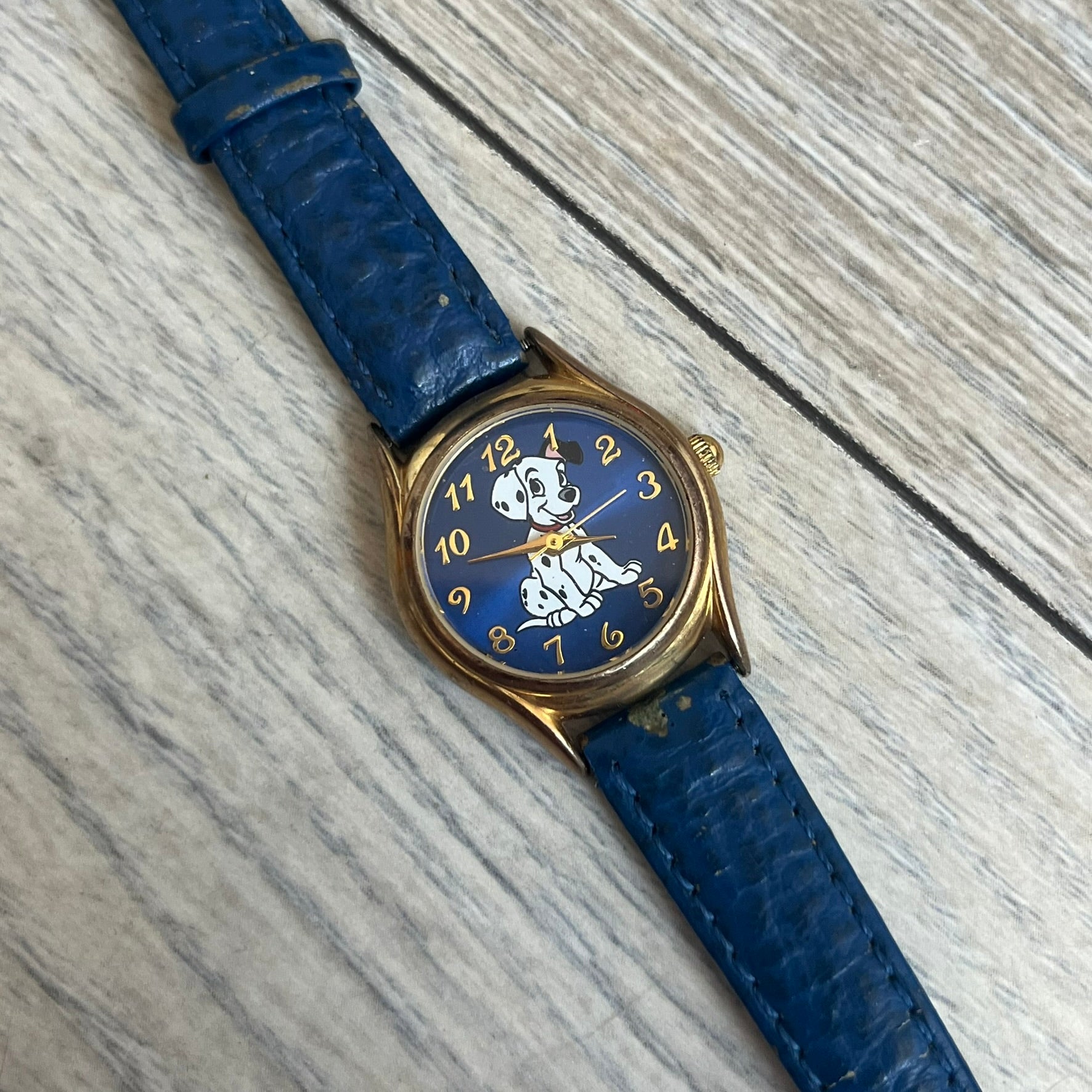 Disney 101 Dalmatians 1990s Blue Analog Watch features a navy leather strap, gold-tone case, and navy dial. The dial includes gold hour markers and hands with a Dalmatian character graphic in the center. The case back is marked as made exclusively for the Disney Store and includes a Japan movement marking. The watch is sized for smaller wrists.

