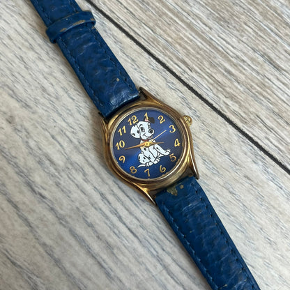 Disney 101 Dalmatians 1990s Blue Analog Watch features a navy leather strap, gold-tone case, and navy dial. The dial includes gold hour markers and hands with a Dalmatian character graphic in the center. The case back is marked as made exclusively for the Disney Store and includes a Japan movement marking. The watch is sized for smaller wrists.
