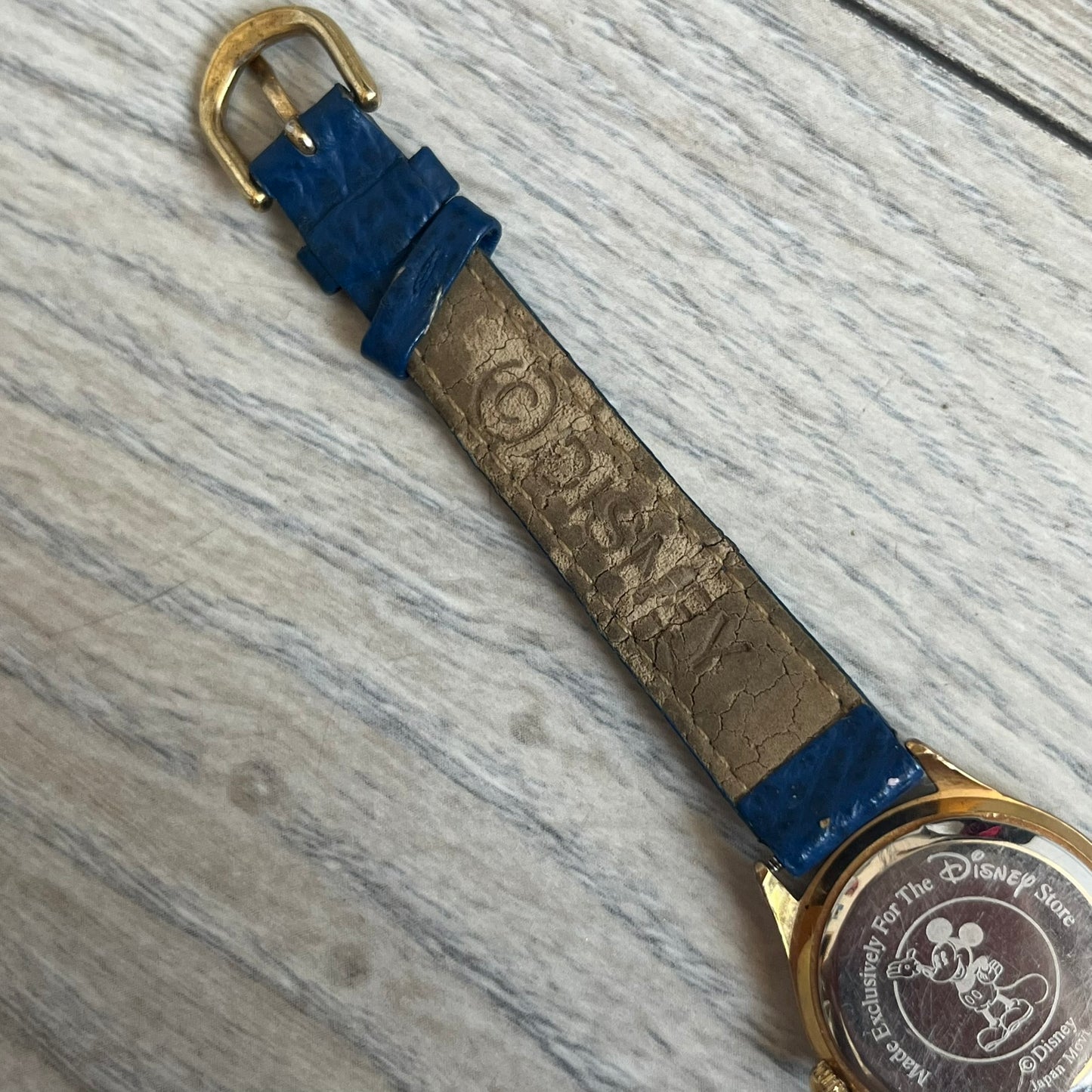 Disney 101 Dalmatians 1990s Blue Analog Watch features a navy leather strap, gold-tone case, and navy dial. The dial includes gold hour markers and hands with a Dalmatian character graphic in the center. The case back is marked as made exclusively for the Disney Store and includes a Japan movement marking. The watch is sized for smaller wrists.
