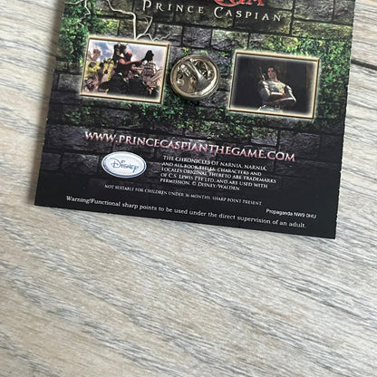 Disney 2008 The Chronicles of Narnia: Prince Caspian Pin is a silver-tone metal pin featuring a red lion with a yellow crown. The pin is attached to a promotional backing card displaying characters from The Chronicles of Narnia: Prince Caspian, the game title, and “The Video Game” text. The reverse side of the card contains additional game information and licensing details.