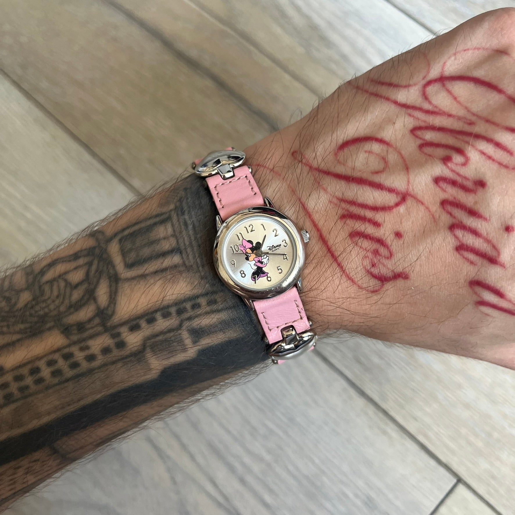 Disney Mickey Mouse 1990s Pink Analog Watch features a pink leather bracelet with metal heart details connecting sections of the strap. It has a silver-tone case and a silver dial with matching silver hour markers and hands. The center of the dial features a Mickey Mouse graphic with a small Disney logo beside it. The back includes a Time Works logo and Japan movement marking. The watch is sized for smaller wrists.
