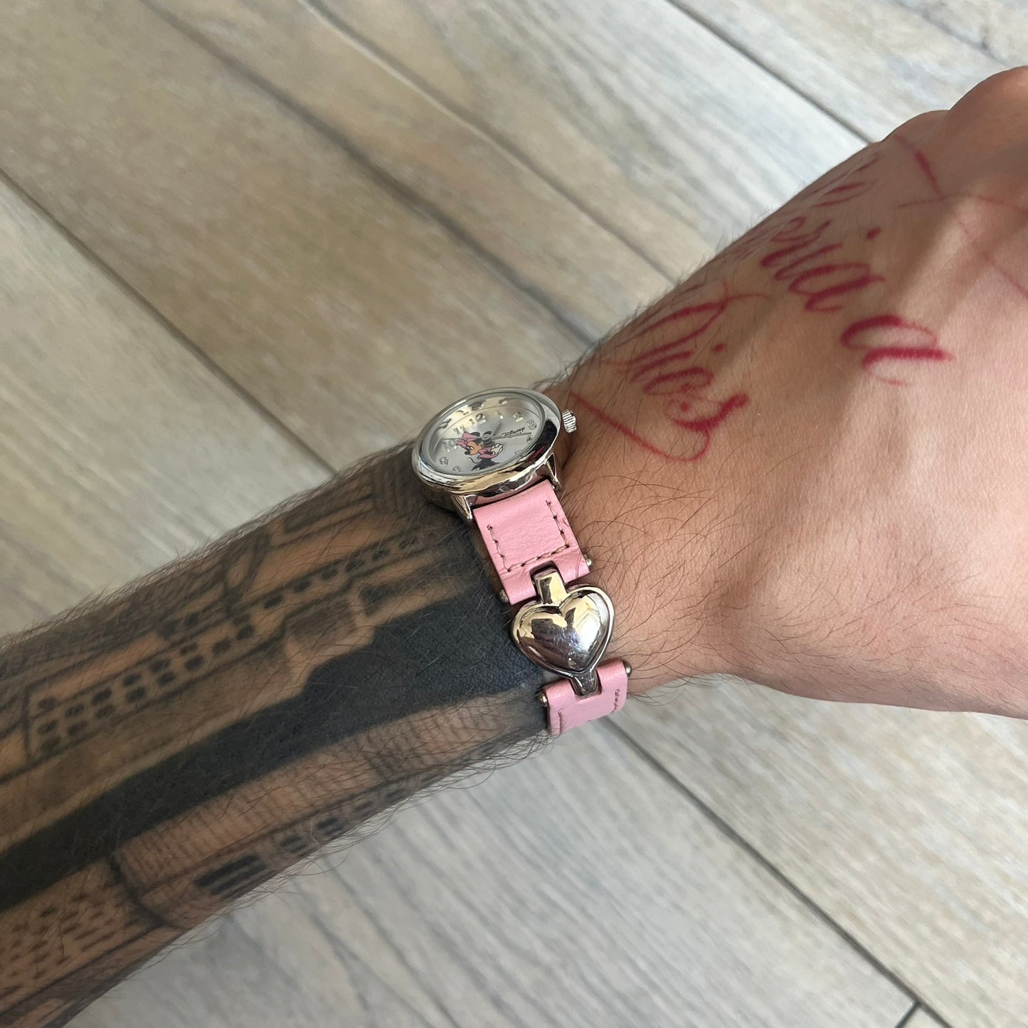 Disney Mickey Mouse 1990s Pink Analog Watch features a pink leather bracelet with metal heart details connecting sections of the strap. It has a silver-tone case and a silver dial with matching silver hour markers and hands. The center of the dial features a Mickey Mouse graphic with a small Disney logo beside it. The back includes a Time Works logo and Japan movement marking. The watch is sized for smaller wrists.
