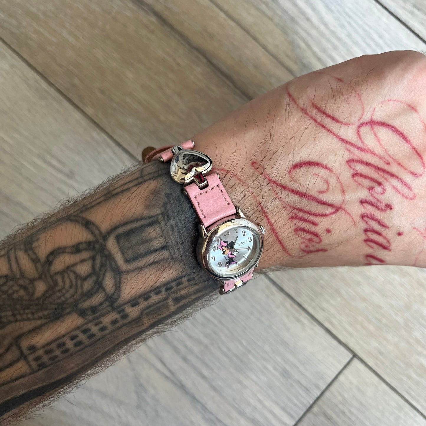 Disney Mickey Mouse 1990s Pink Analog Watch features a pink leather bracelet with metal heart details connecting sections of the strap. It has a silver-tone case and a silver dial with matching silver hour markers and hands. The center of the dial features a Mickey Mouse graphic with a small Disney logo beside it. The back includes a Time Works logo and Japan movement marking. The watch is sized for smaller wrists.
