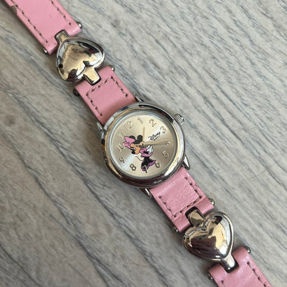 Disney Mickey Mouse 1990s Pink Analog Watch features a pink leather bracelet with metal heart details connecting sections of the strap. It has a silver-tone case and a silver dial with matching silver hour markers and hands. The center of the dial features a Mickey Mouse graphic with a small Disney logo beside it. The back includes a Time Works logo and Japan movement marking. The watch is sized for smaller wrists.
