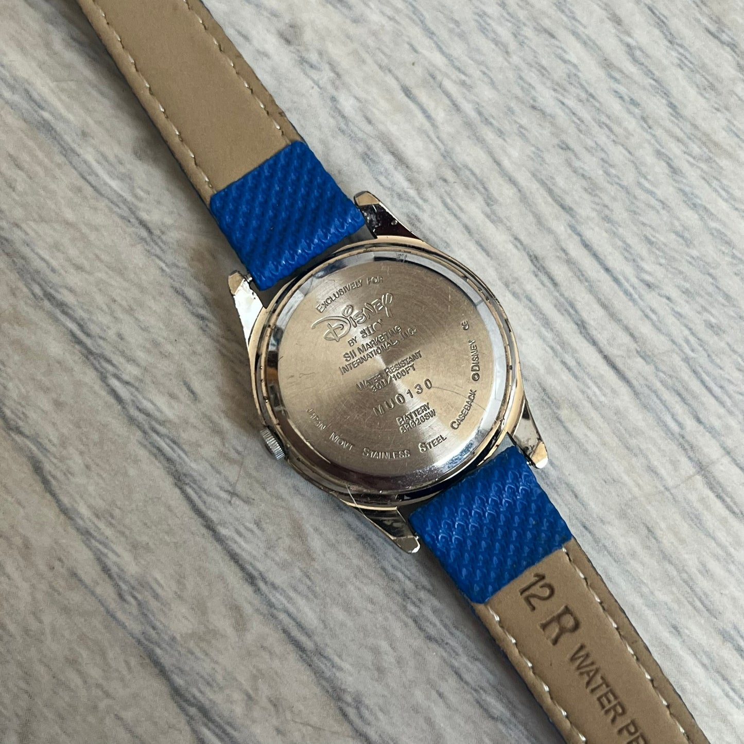 Disney Winnie-the-Pooh 1990s Analog Watch features blue leather straps, a gold-tone case, and a navy dial. The dial displays gold hour markers with Winnie the Pooh illustrated in the center. The case back is marked with official Disney licensing and indicates it was made exclusively for Disney. This watch is sized for smaller wrists.
