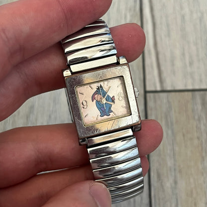 Disney Winnie-the-Pooh Eeyore 1990's Analog Watch is a stainless steel watch with a shiny finish and a stretch expansion bracelet made from connected metal links. The dial features silver numerals with a graphic of Eeyore. The caseback includes "Exclusively for Disney". Bracelet is for smaller wrists.
