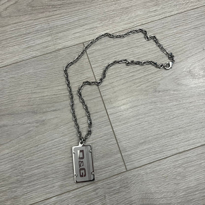 Dolce &amp; Gabbana Propaganda Dog Tag Necklace, featuring a silver stainless steel square tag with four visible screws and the D&amp;G logo engraved on the front. The tag hangs from a durable cable chain, combining sturdy construction with clean, industrial-inspired detailing.