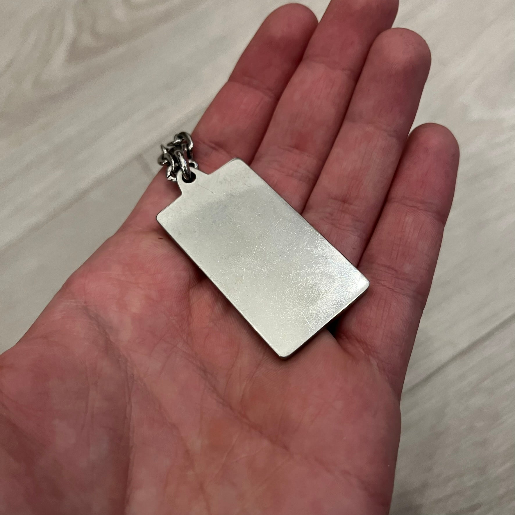 Dolce &amp; Gabbana Propaganda Dog Tag Necklace, featuring a silver stainless steel square tag with four visible screws and the D&amp;G logo engraved on the front. The tag hangs from a durable cable chain, combining sturdy construction with clean, industrial-inspired detailing.