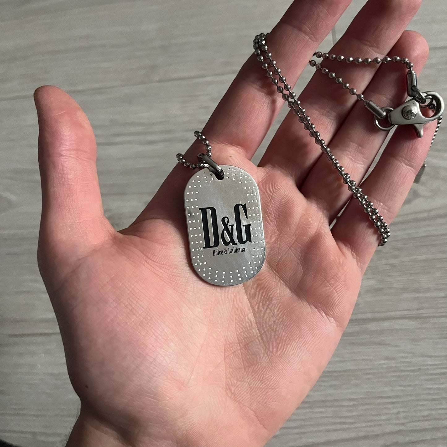 Dolce &amp; Gabbana Cowboy Dog Tag Necklace, model DJ0633. Features a silver-tone metal ball chain and a dog tag with black cowboy-style D&amp;G logo and small “Dolce &amp; Gabbana” text underneath. The front of the tag is patterned with subtle white dots for added detail.